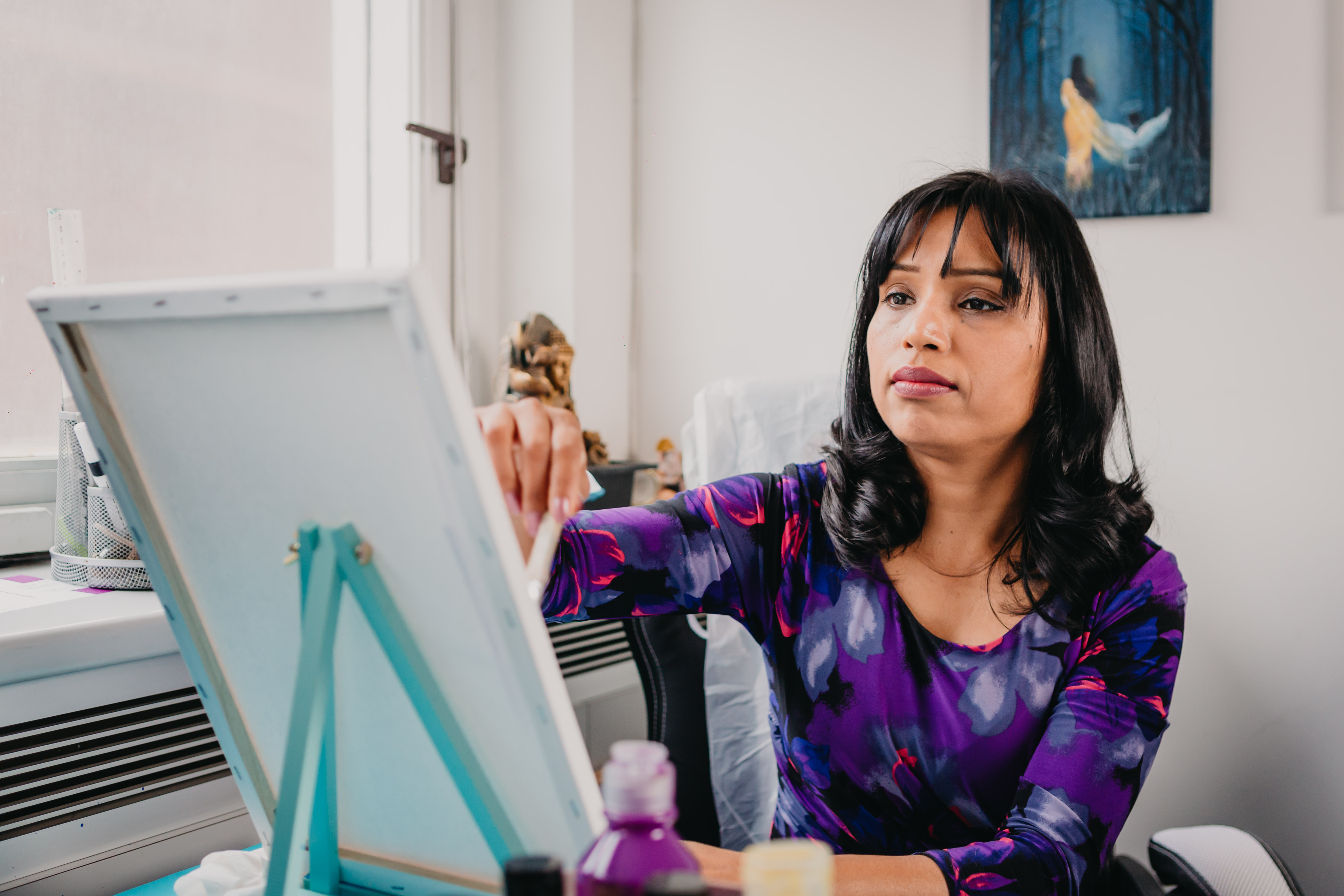 A woman in a purple top paints at a table top easel